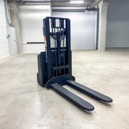 Pelēks ar melnu Elektriskais grēdotājs FORK EG15-20 palešu pacelšanai noliktavā. Skats no sāniem ar nolaistām dakšām